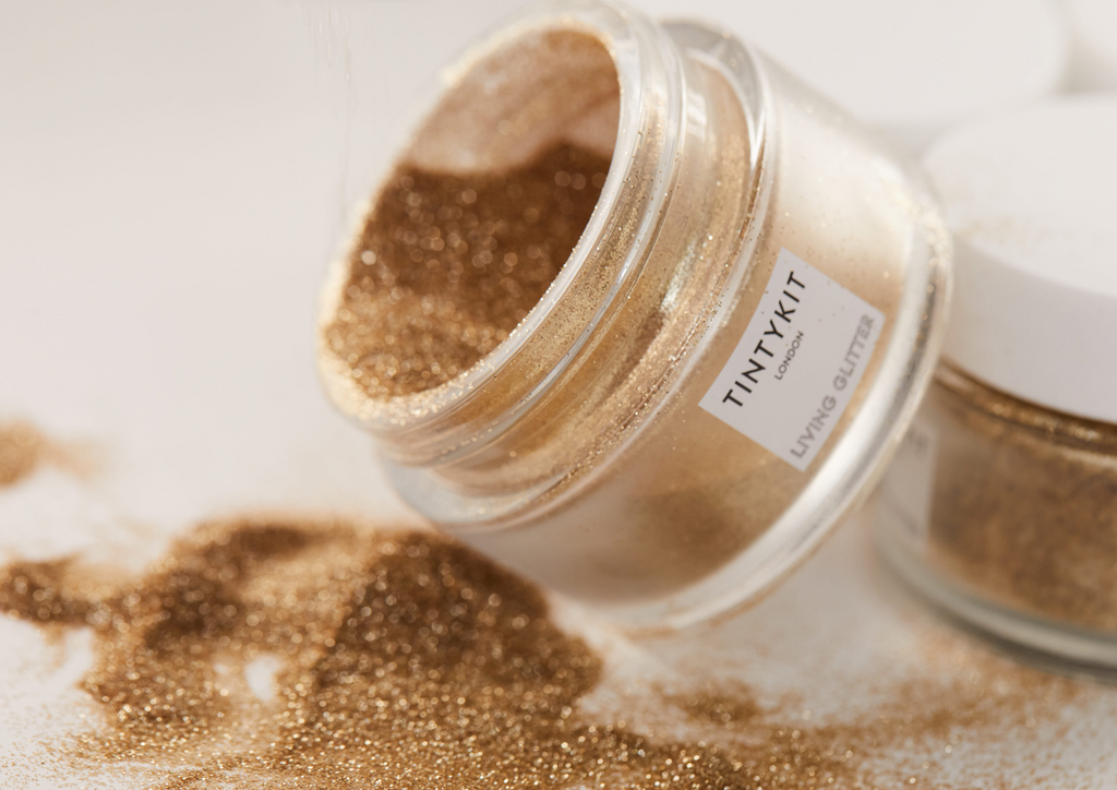 Product image of TINTYKIT LIVING GLITTER biodegradable glitter. Product variant: Gold Stardust. Open jar with glitter being poured on table.