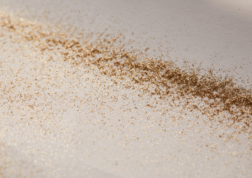 Product image of TINTYKIT LIVING GLITTER biodegradable glitter. Product variant: Gold Stardust. Artistic view of glitter sprinkled on table.