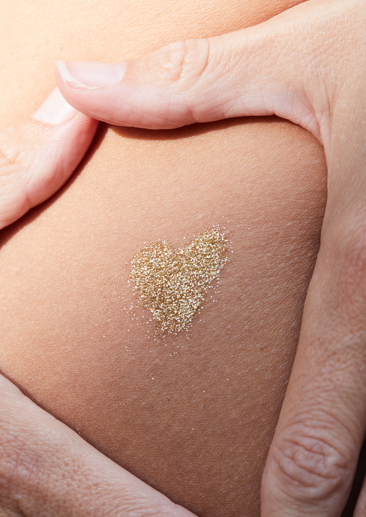 Product image of TINTYKIT LIVING GLITTER biodegradable glitter. Product variant: Gold Stardust. Artistic view of glitter painted in a heart shape on a woman's skin.